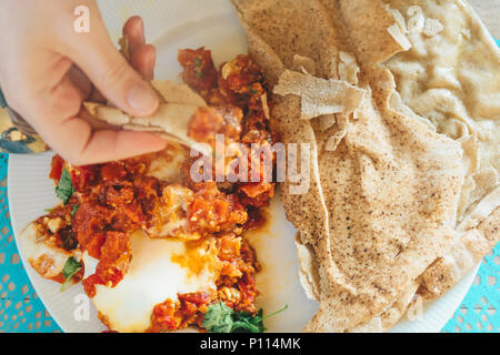 Stretta di mano femmina mangiare medio orientale shakshouka piatto con flatbread Foto Stock