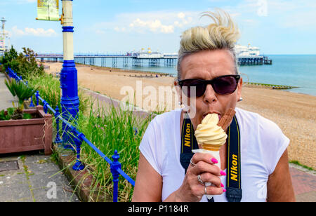 Donna di mezza età a mangiare il gelato in riva al mare Foto Stock