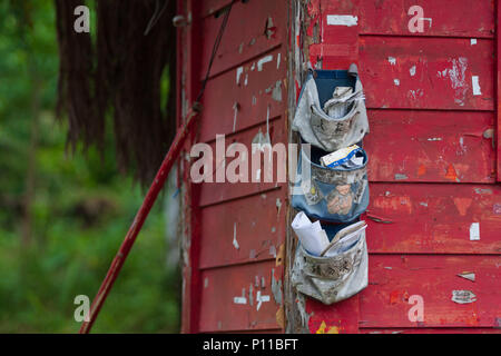 Buste ordinati nella parete appesi Sacchetti di stoccaggio. Mail in tasca organizer borse, dipinta di rosso rustico parete in legno all'esterno. Foto Stock