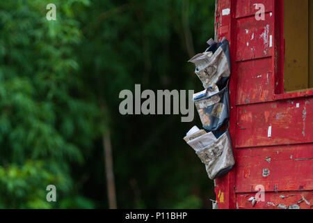 Buste ordinati nella parete appesi Sacchetti di stoccaggio. Mail in tasca organizer borse, dipinta di rosso rustico parete in legno all'esterno. Foto Stock