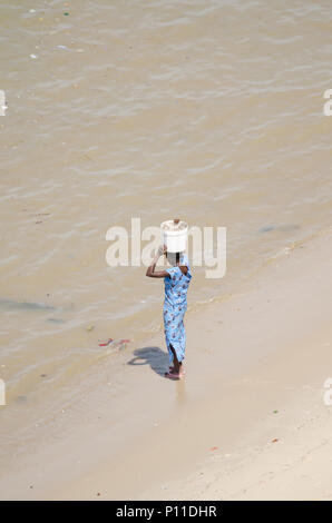 Unidentified donna africana in vestito blu permanente sulla spiaggia della benna di bilanciamento Foto Stock