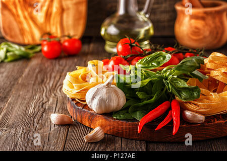 Prodotti per la cucina - pasta, pomodori, aglio, pepe e basilico sul vecchio sfondo di legno. Foto Stock