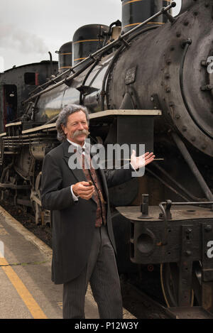 Una guida turistica, vestito come Mark Twain, pone accanto a un treno a vapore in Essex Connecticut Foto Stock