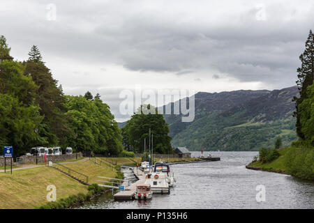 Fort Augustus, Scozia - Giugno 11, 2012: Argento Oich Canal con imbarcazione da diporto dock si svuota in Loch Ness, fiancheggiata da verdi foreste su colline all'hori Foto Stock