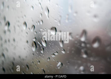 Primo piano di gocce di pioggia sulla finestra di fronte sullo sfondo della città Foto Stock