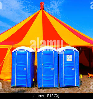 Rosso e giallo marquee contro il cielo blu con blu bagni portatili sul lato anteriore Foto Stock