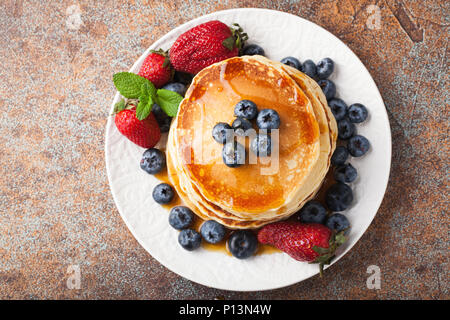 Close-up deliziosi pancake con mirtilli freschi, fragole e sciroppo d'acero su un sfondo arrugginito. Con copia spazio. Vista dall'alto. Foto Stock