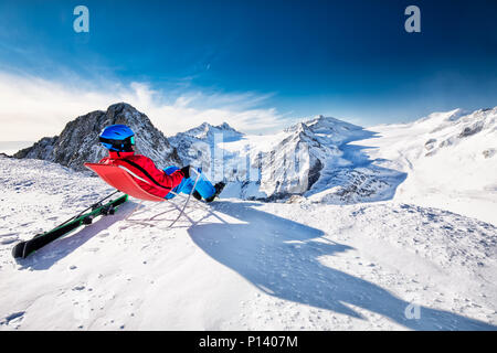 Giovane sciatore felice seduto sulla cima delle montagne godendo la vista dal ghiacciaio Presena, Tonale, Italia Foto Stock