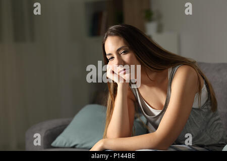 Somnolent donna che guarda la fotocamera nella notte seduto su un divano nel salotto di casa Foto Stock