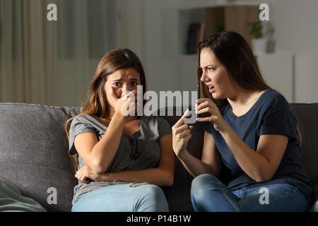 Ragazza scolding il suo triste amico circa i contenuti multimediali seduta su un divano nel salotto di casa Foto Stock