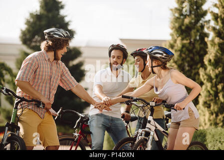 Gruppo di giovani felici i ciclisti di riposo in posizione di parcheggio. Quattro simpatici amici mettendo le mani insieme nel parco, bella giornata d'estate. Concetto di estate felice "vacatio Foto Stock