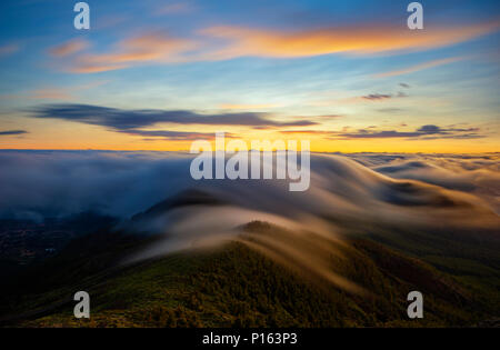 Un magnifico spettacolo delle nuvole che fluisce oltre le montagne al tramonto su Tenerife Foto Stock