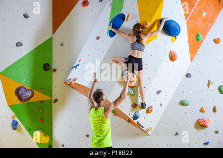 Arrampicatori in palestra di arrampicata. Giovane donna climbing bouldering problema (route), istruttore di sesso maschile che fissano la sua. Foto Stock