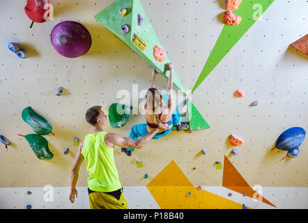 Arrampicatori in palestra di arrampicata. Giovane donna climbing bouldering problema (route), istruttore di sesso maschile che fissano la sua. Foto Stock