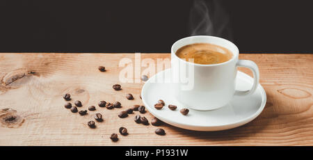 Tazza di caffè fumante e chicchi di caffè tostati su tavola in legno rustico con sfondo scuro. Copia dello spazio. Foto Stock