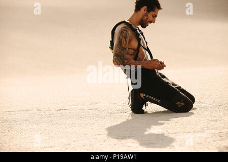 Giovane uomo che un riposo dopo allenamento sulla sabbia del deserto. Montare l'uomo relax dopo un allenamento intenso all'esterno. Foto Stock