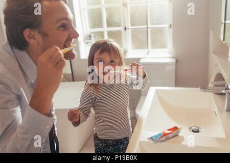 Padre e figlia spazzolare i denti in piedi in bagno. L'uomo ad insegnare la sua figlia come spazzolare i denti. Foto Stock