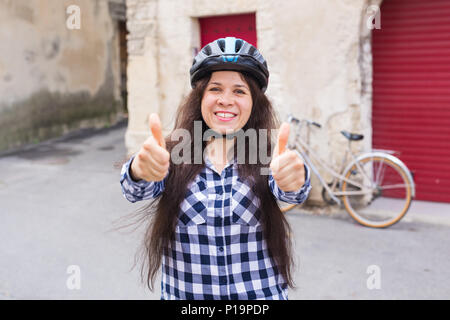 Bellezza donna allegra dando pollice in alto sulla bicicletta e porte rosso sfondo. Foto Stock