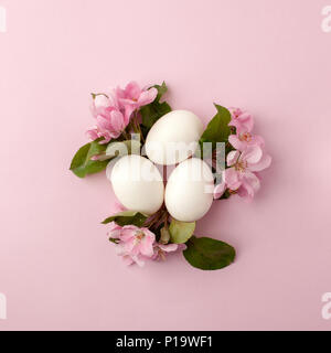 Uova di Pasqua e fiori di colore rosa su sfondo bianco. Nido di pasqua. Appartamento laico, vista dall'alto, il concetto di molla, la femminilità e la bellezza. Foto Stock