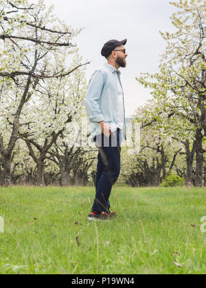 Tanga barbuto uomo di indossare un abbigliamento informale e occhiali da sole godendo di una passeggiata nella natura Foto Stock