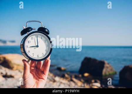 Tenere in mano guarda sulla spiaggia sfondo.sveglia sul mare e Sfondo sabbia diverso tempo con le vacanze estive.Tempo di vacanza concept Foto Stock