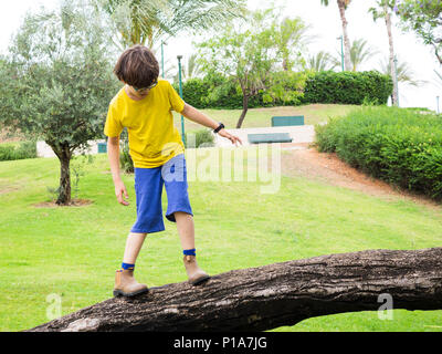 Giovane ragazzo di dieci in giallo t-shirt e blu pantaloni larghi gioca da solo in un giardino. Modello di rilascio disponibili Foto Stock