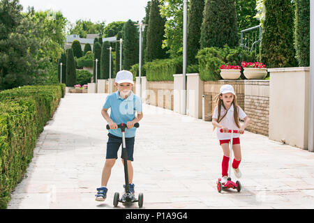 Preschooler ragazzo e una ragazza scooter equitazione all'esterno. Foto Stock