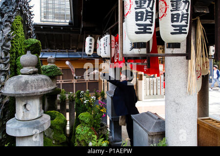 Un adoratore schizza acqua su una divinità Shintoista statua presso il Tempio Hozenji, Osaka, Giappone Foto Stock