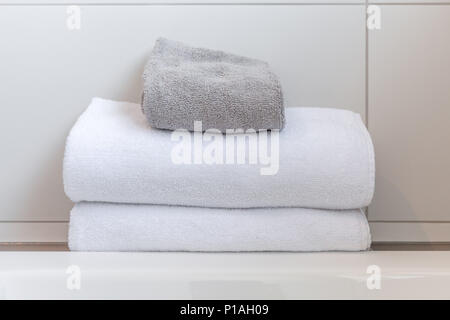 Bianco e grigio asciugamani ripiegati contro le piastrelle bianche nella stanza da bagno Foto Stock
