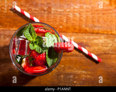 Estate bevanda fredda con le fragole, menta e ghiaccio in vetro su sfondo di legno. Vista dettagliata del cocktail con un fresco e bacche. Foto Stock