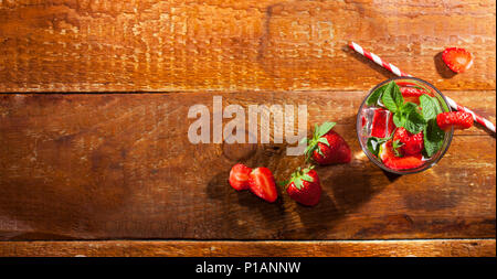 Estate bevanda fredda con le fragole, menta e ghiaccio in vetro su sfondo di legno. Vista dettagliata del cocktail con un fresco e bacche. Foto Stock