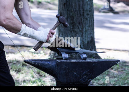 Processo di fabbricazione di medievale arma ax. Fabbro manualmente le mani forgiatura sull'incudine con martello. Close up, il fuoco selettivo Foto Stock