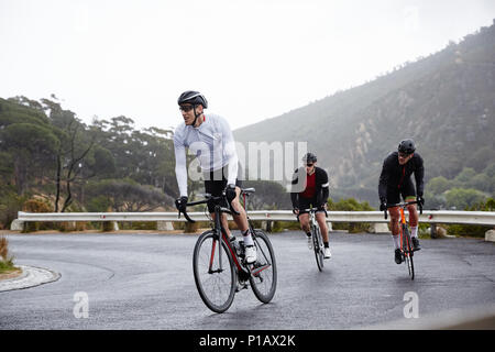 I ciclisti di sesso maschile il ciclismo in salita su strada bagnata Foto Stock