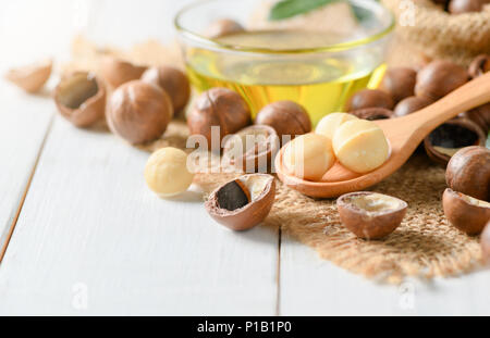 Noci di Macadamia sul cucchiaio di legno e noci macadamia Olio su legno bianco sullo sfondo di legno. super e cibo sano concetto, Foto Stock