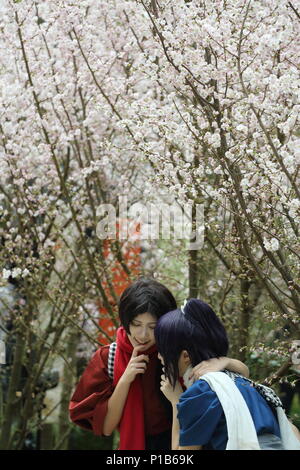 Due giocatori cosplay che posano per una foto di fronte al bianco alberi sakura a giardini dalla Baia di Singapore. Foto Stock