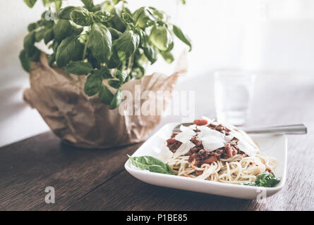 Close-up di di pasta con il ragù alla Bolognese, basilico e parmigiano grattugiato su tavola in legno rustico Foto Stock