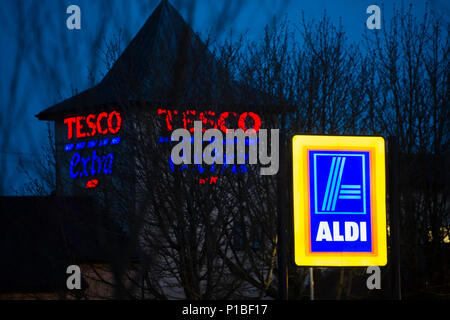 Aldi convenienti supermercati logo illuminato segno, con Tesco supernarket in background, esterna, notte, Cirencester Inghilterra REGNO UNITO Foto Stock