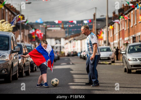 Iris nella parte occidentale di Belfast residente Turley sabbiosa e suo figlio Aaron Turley giocando a calcio per strada come lui e altri residenti hanno ottenuto in Coppa del Mondo febbre a creare un gioco a premi e raccogliere fondi per una festa di strada il giorno della finale della Coppa del mondo. Foto Stock