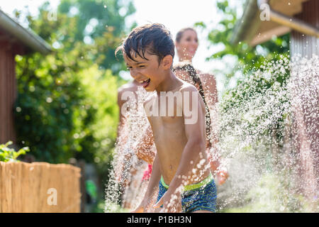 Ragazzo il raffreddamento con tubo flessibile da giardino, famiglia in background Foto Stock