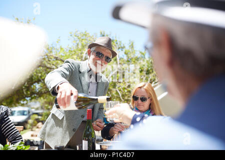 Senior uomo in tuta e bow tie versando il vino per gli amici a sunny garden party Foto Stock