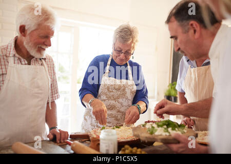 Attiva gli amici senior rendendo la pizza in classe di cucina Foto Stock