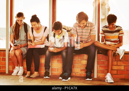 Felice gli studenti seduti sul davanzale e utilizzando il telefono cellulare nel corridoio Foto Stock