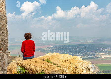Una donna si siede su una montagna e guarda verso il basso in corrispondenza dei campi e del villaggio. Monte Ghilboa in Israele. Foto Stock