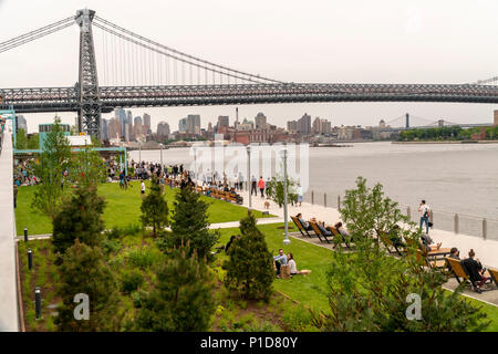 Nonostante il tempo inclemente di migliaia di visitatori accorsi per la grande apertura di Domino Parco nel quartiere di Williamsburg di Brooklyn a New York Domenica, 10 giugno 2018. Occupa il sito del Domino Sugar Co. raffineria, chiusa nel 2004, cinque acri di greenspace ha caratteristiche di acqua, scivoli, una passerella elevata, un Danny Meyer stand alimentari e pallavolo come pure molte altre dotazioni. Progettato da James Corner Field Operations, gli architetti dietro il design della linea alta, la raffineria di mattone di edificio, di cui una volta elaborato il 50 percento di tutto lo zucchero negli Stati uniti rimane per de Foto Stock