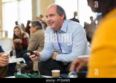 Imprenditore sorridente utilizzando smart phone a una conferenza Foto Stock