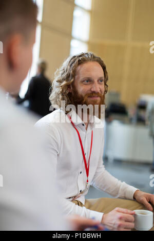 Imprenditore sorridente di bere il caffè a una conferenza Foto Stock