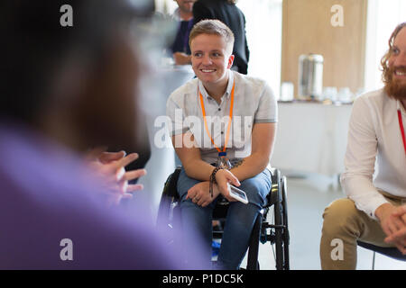 Donna sorridente in carrozzella a parlare con i colleghi in conferenza Foto Stock