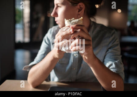 La donna è seduta nel piccolo caffè e azienda Tortilla avvolgere prima di mangiare, guardando a parte. Foto Stock