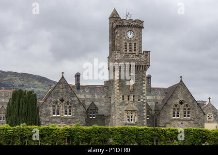 Fort Augustus, Scozia - Giugno 11, 2012: Closeup dell'Abbazia Highland Club con la torre dell orologio fronteggiata da giardino sotto pesante cloudscape. Le colline sulla orizz. Foto Stock