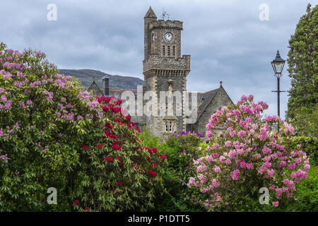 Fort Augustus, Scozia - Giugno 11, 2012: Closeup dell'Abbazia Highland Club torre dell orologio con fiori fronteggiata da giardino sotto pesante cloudscape. Foto Stock